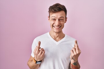 Caucasian man standing over pink background showing middle finger doing fuck you bad expression,...
