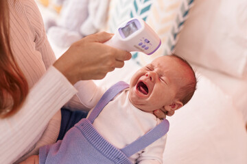 Mother and son measuring fever using thermometer at home
