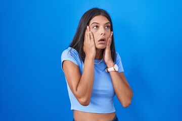 Brunette young woman standing over blue background tired hands covering face, depression and sadness, upset and irritated for problem