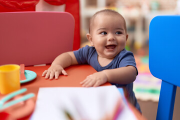 Adorable chinese toddler leaning on table standing at kindergarten