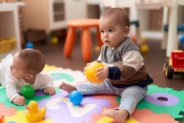 Two adorable toddlers playing with balls sitting on floor at kindergarten - Powered by Adobe