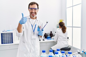 Middle age man working at scientist laboratory smiling happy and positive, thumb up doing excellent and approval sign