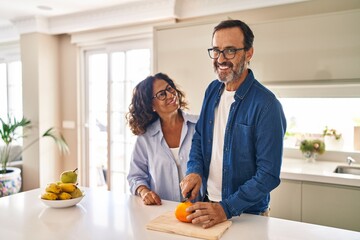Middle age hispanic couple smiling confident cutting orange at kitchen