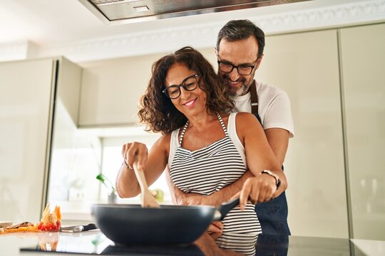 Middle age hispanic couple smiling confident and hugging each other cooking at kitchen