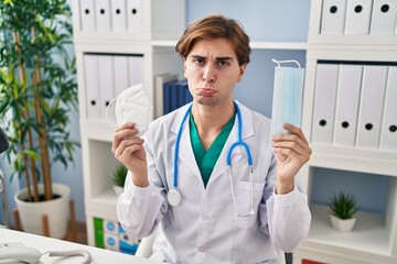 Young doctor man holding two safety mask depressed and worry for distress, crying angry and afraid....