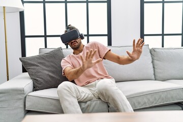 Fototapeta premium Handsome hispanic man afraid wearing virtual reality glasses at the living room at home