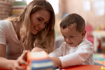 Obraz premium Teacher and toddler playing with cars toy sitting on table at kindergarten