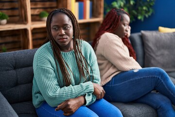 African american women friends sitting on sofa with disagreement expression at home