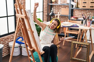 Young beautiful hispanic woman artist listening to music and dancing at art studio