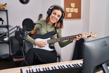 Young beautiful hispanic woman musician playing electrical guitar at music studio