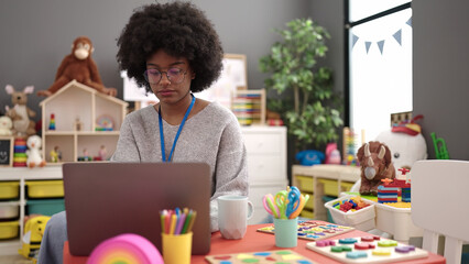 African american woman preschool teacher using laptop sitting on table at kindergarten