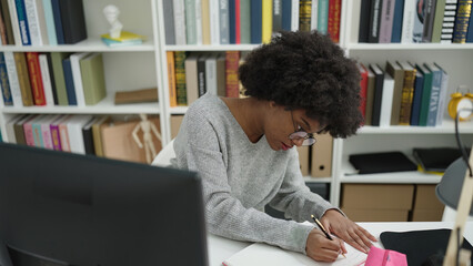 African american woman student using computer writing on notebook at library university