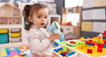 Adorable hispanic toddler holding elephant toy standing at kindergarten