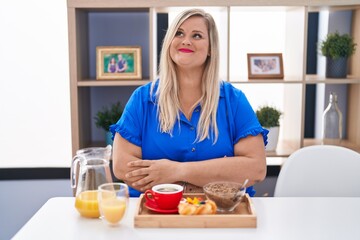 Obraz na płótnie Canvas Caucasian plus size woman eating breakfast at home smiling looking to the side and staring away thinking.