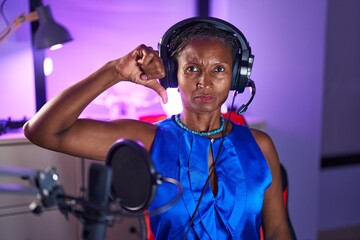 African woman with dreadlocks wearing headphones with angry face, negative sign showing dislike with thumbs down, rejection concept