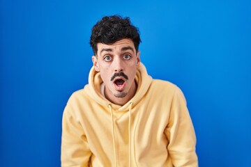 Fototapeta premium Hispanic man standing over blue background afraid and shocked with surprise and amazed expression, fear and excited face.