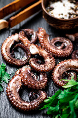 Pieces of fresh octopus on a stone board with greenery. 