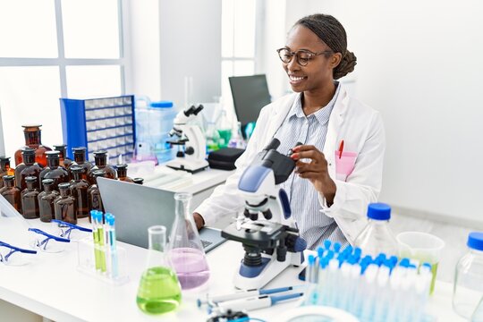 African american woman scientist using laptop and microscope at laboratory