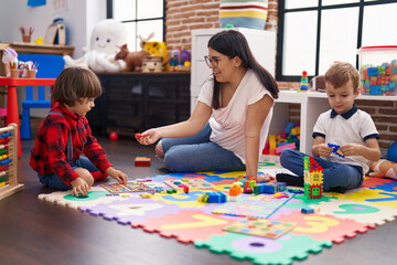 Teacher with boys playing with maths puzzle game sitting on floor at kindergarten
