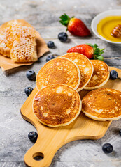 Homemade pancakes on a cutting board with honey and berries. 