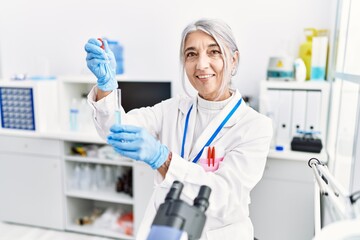 Middle age grey-haired woman wearing scientist uniform using pipette at laboratory