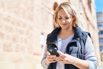 Fototapeta premium Young blonde woman smiling confident using smartphone at street