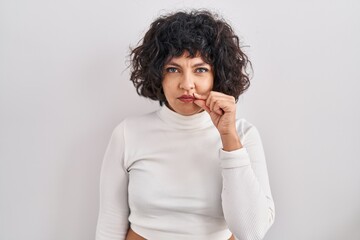 Fototapeta na wymiar Hispanic woman with curly hair standing over isolated background mouth and lips shut as zip with fingers. secret and silent, taboo talking