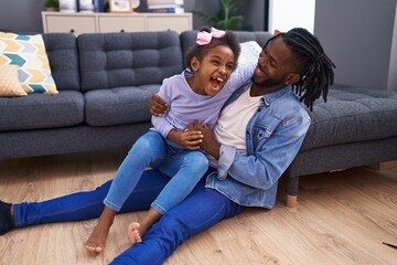Father and daughter sitting on floor together laughing for tickles at home
