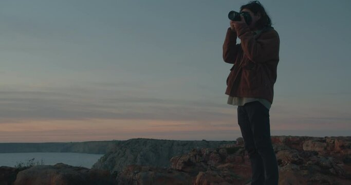 Long haired male photographer taking pictures and enjoying the scenery during sunset and blue hour on the coastline, cliffs of the Algarve, Portugal