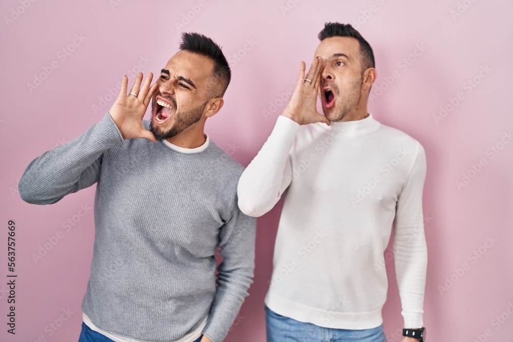 Sticker Homosexual couple standing over pink background shouting and screaming loud to side with hand on mouth. communication concept.