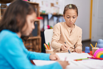 Two kids students sitting on table drawing on paper at kindergarten