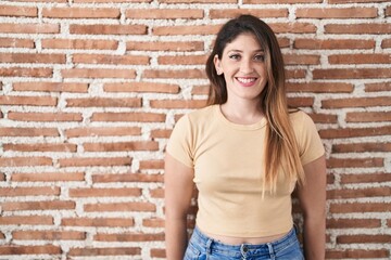 Young brunette woman standing over bricks wall with a happy and cool smile on face. lucky person.