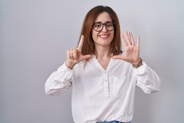 Brunette woman standing over white isolated background showing and pointing up with fingers number seven while smiling confident and happy.