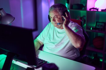 Middle age grey-haired man streamer playing video game using computer at gaming room