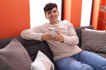 Non binary man using smartphone sitting on sofa at home