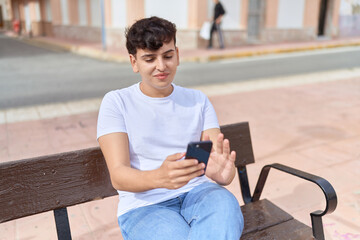 Obraz premium Non binary man using smartphone sitting on bench at park