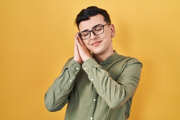Fototapeta premium Non binary person standing over yellow background sleeping tired dreaming and posing with hands together while smiling with closed eyes.