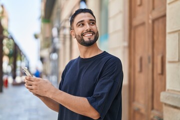 Young arab man smiling confident using smartphone at street