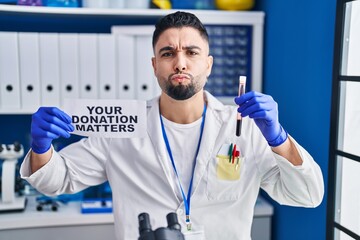 Young handsome man working at scientist laboratory holding blood sample looking at the camera...