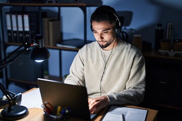 Fototapeta premium Young handsome man working using computer laptop at night relaxed with serious expression on face. simple and natural looking at the camera.