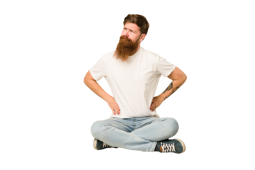 Young adult redhead with a long beard sitting on the floor isolated confused, feels doubtful and unsure.