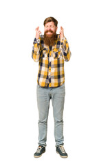 Young adult redhead man with a long beard standing full body isolated crossing fingers for having luck