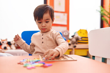 Adorable hispanic boy playing with maths puzzle game sitting on table at kindergarten