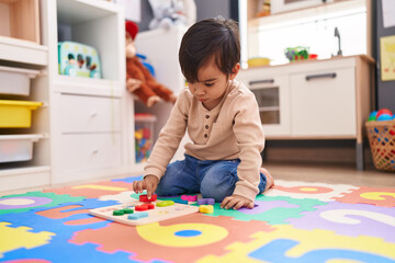 Adorable hispanic boy playing with maths puzzle game sitting on floor at kindergarten