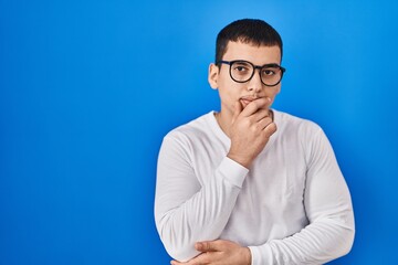 Obraz premium Young arab man wearing casual white shirt and glasses looking confident at the camera with smile with crossed arms and hand raised on chin. thinking positive.