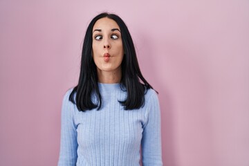 Fototapeta premium Hispanic woman standing over pink background making fish face with lips, crazy and comical gesture. funny expression.