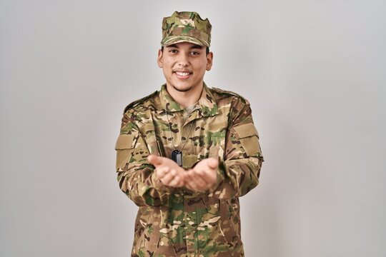 Young arab man wearing camouflage army uniform smiling with hands palms together receiving or giving gesture. hold and protection