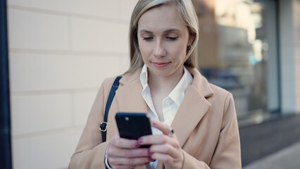 Young blonde woman using smartphone standing at street