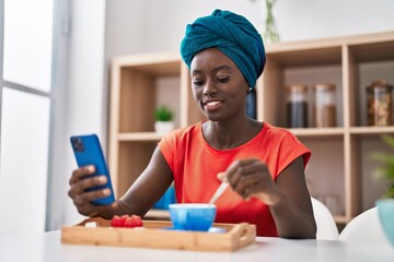 Young african american woman using smartphone having breakfast at home