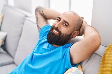 Young bald man relaxed with hands on head sitting on sofa at home